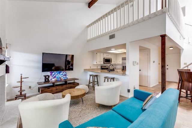 living area with visible vents, baseboards, a towering ceiling, beamed ceiling, and a brick fireplace