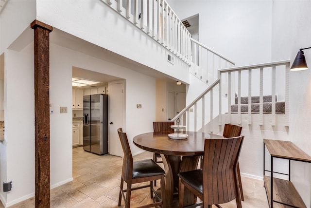 dining area with stone tile floors, a towering ceiling, baseboards, visible vents, and stairway