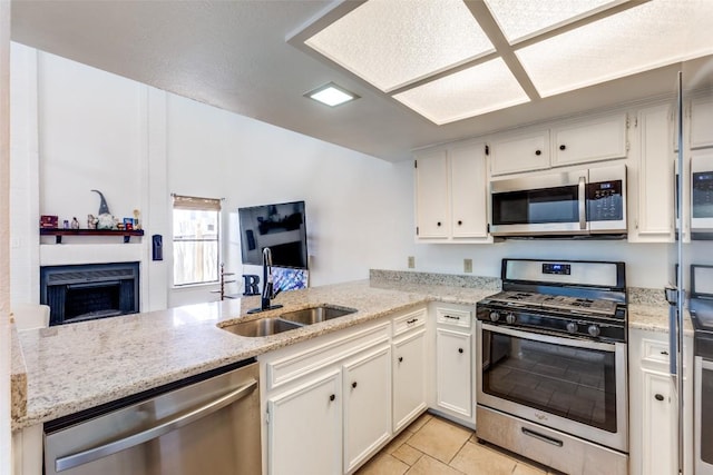 kitchen with a fireplace, a sink, a peninsula, appliances with stainless steel finishes, and white cabinetry