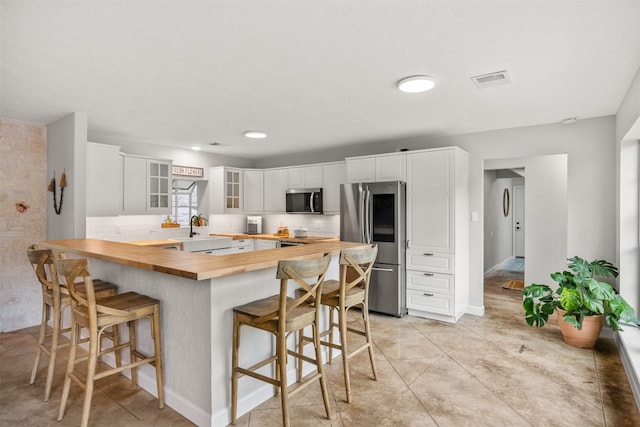 12099 Bonham Ranch Rd, Dripping Springs, TX 78620 - kitchen featuring wooden counters, appliances with stainless steel finishes, glass insert cabinets, a breakfast bar area, and decorative backsplash