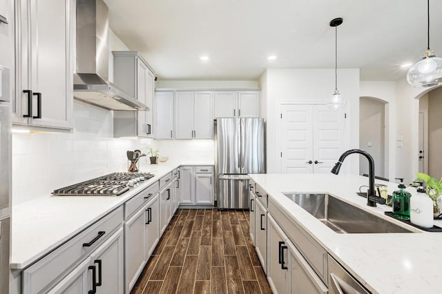 kitchen with wall chimney range hood, a sink, stainless steel appliances, arched walkways, and dark wood finished floors
