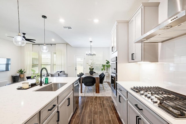 kitchen featuring wall chimney range hood, a sink, visible vents, stainless steel appliances, and backsplash