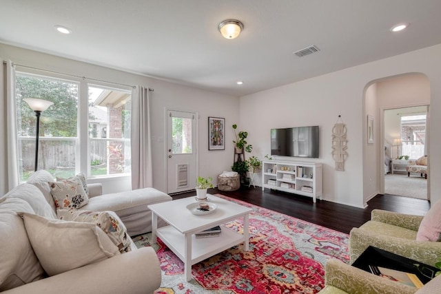 living area with arched walkways, dark wood-type flooring, and recessed lighting