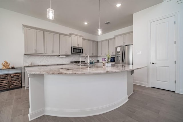 3049 Sage Ranch Dr, Leander, TX 78641 - kitchen featuring stainless steel appliances, wood finished floors, a large island with sink, light stone countertops, and pendant lighting