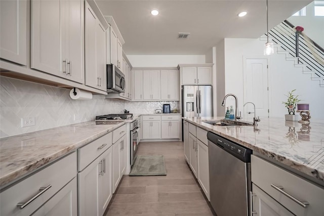3049 Sage Ranch Dr, Leander, TX 78641 - kitchen featuring stainless steel appliances, light wood-style flooring, hanging light fixtures, light stone counters, and backsplash