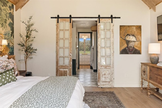bedroom with a barn door, vaulted ceiling, wood finished floors, and baseboards