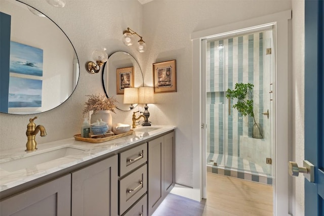 bathroom featuring wood finished floors, a sink, double vanity, and a stall shower