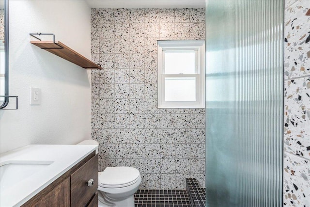 full bathroom featuring a tile shower, vanity, and toilet