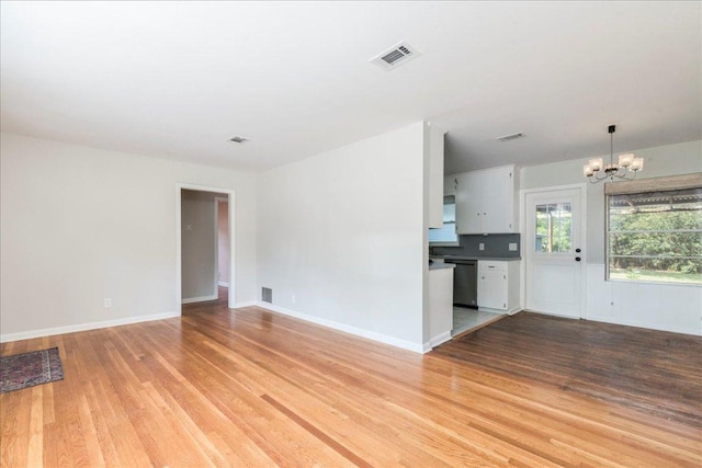 unfurnished living room featuring visible vents, an inviting chandelier, and light wood-style floors