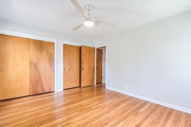 unfurnished bedroom with baseboards, a ceiling fan, wood finished floors, and multiple closets