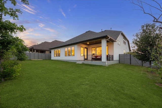 back of property at dusk with stucco siding, a fenced backyard, and a lawn