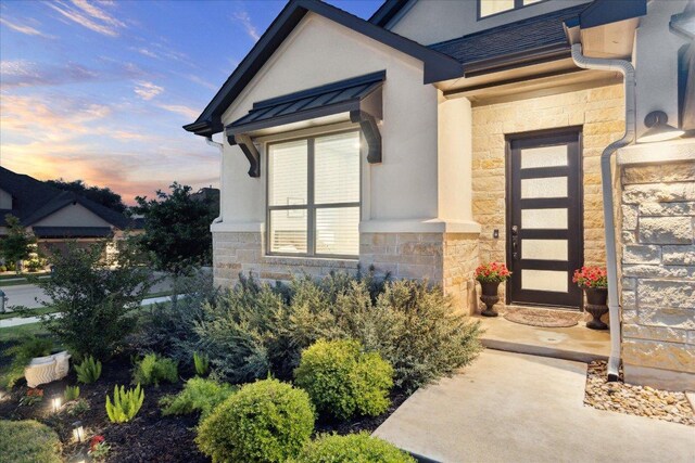 exterior entry at dusk featuring stone siding and stucco siding