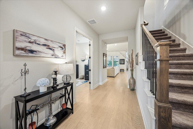 foyer entrance with baseboards, light wood-type flooring, visible vents, and stairs