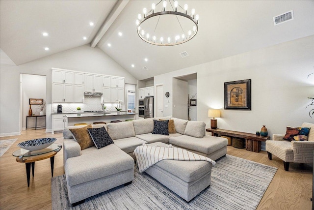living area with beam ceiling, light wood-type flooring, visible vents, an inviting chandelier, and high vaulted ceiling