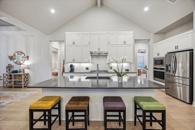 kitchen with under cabinet range hood, dark countertops, a breakfast bar area, and stainless steel appliances