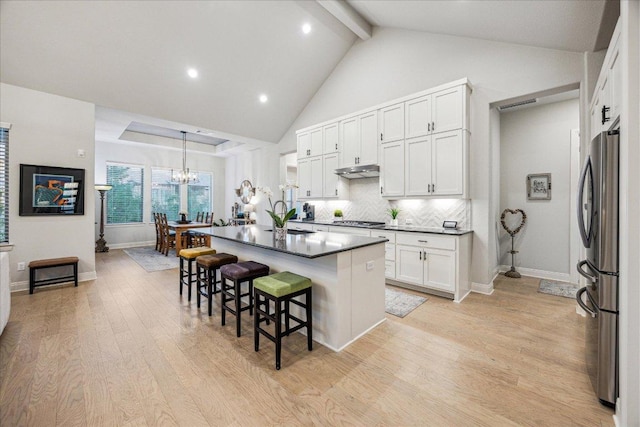 kitchen featuring dark countertops, cooktop, a breakfast bar, under cabinet range hood, and freestanding refrigerator