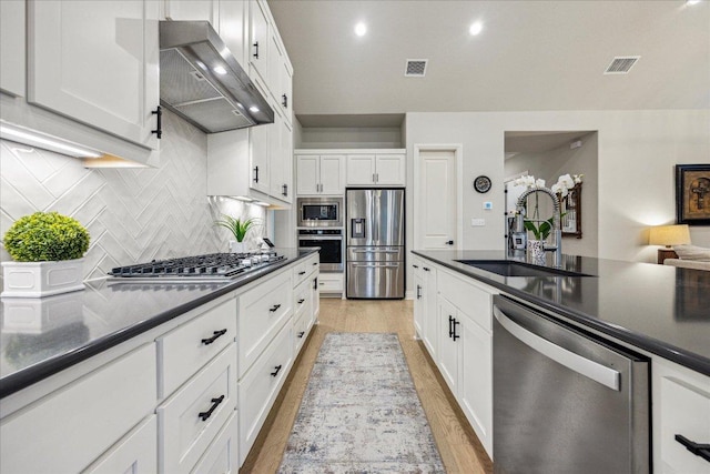 kitchen with exhaust hood, dark countertops, visible vents, a sink, and appliances with stainless steel finishes