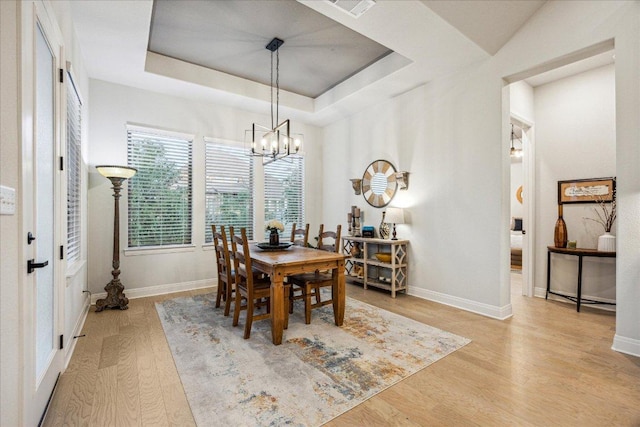 dining room featuring a tray ceiling, wood finished floors, visible vents, baseboards, and a chandelier