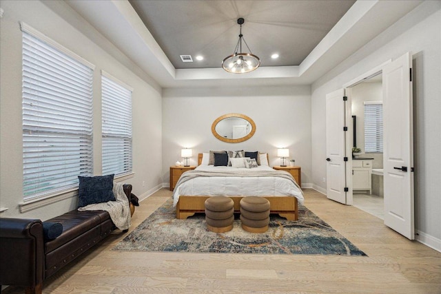 bedroom with light wood finished floors, baseboards, a tray ceiling, and visible vents