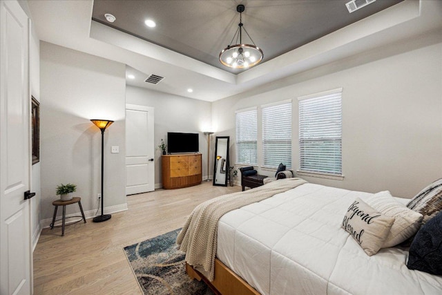 bedroom featuring light wood finished floors, baseboards, visible vents, a chandelier, and a raised ceiling