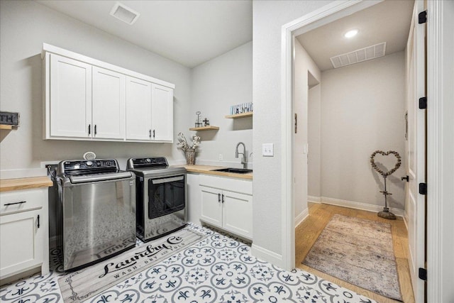 laundry room featuring washing machine and clothes dryer, visible vents, a sink, and cabinet space