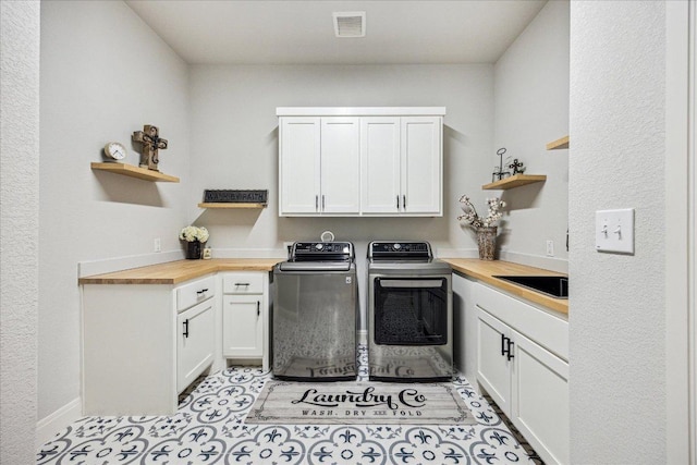 washroom featuring washing machine and clothes dryer, a sink, cabinet space, baseboards, and visible vents