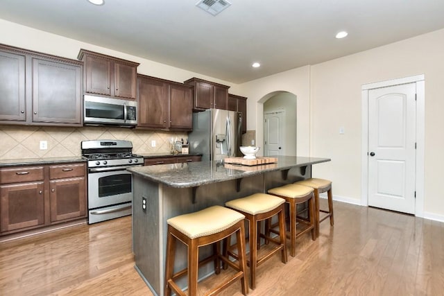 110 Chestnut Ct, Georgetown, TX 78633 - kitchen featuring stainless steel appliances, arched walkways, a kitchen island, a breakfast bar area, and light wood-type flooring