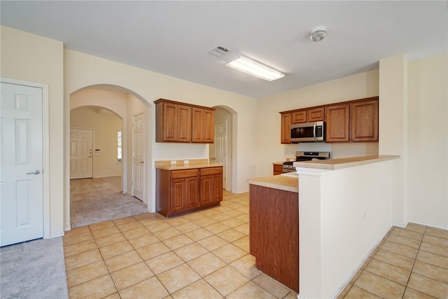 10916 Furrow Hill Dr, Austin, TX 78754 - kitchen featuring appliances with stainless steel finishes, arched walkways, brown cabinets, and light countertops