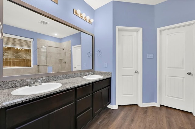 bathroom featuring a stall shower, wood finished floors, double vanity, and baseboards