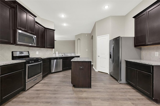 kitchen with stainless steel appliances, a center island, a sink, tasteful backsplash, and dark brown cabinetry