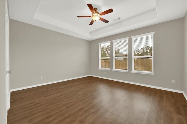 unfurnished room featuring a tray ceiling, baseboards, a ceiling fan, and dark wood-style flooring