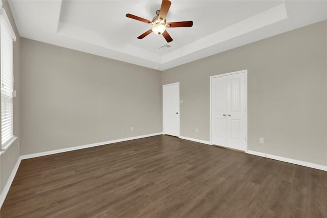 empty room featuring a tray ceiling, a ceiling fan, dark wood-type flooring, and baseboards