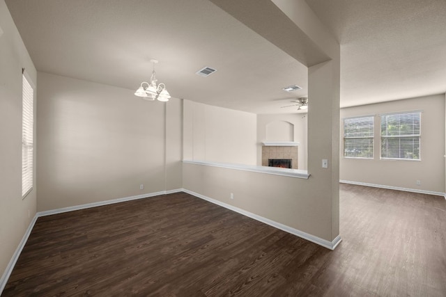 interior space with baseboards, visible vents, ceiling fan with notable chandelier, a fireplace, and dark wood-type flooring