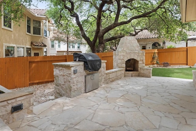 view of patio / terrace with a fenced backyard, exterior fireplace, an outdoor kitchen, and a grill