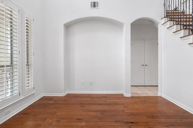 empty room featuring stairway, arched walkways, wood-type flooring, baseboards, and visible vents