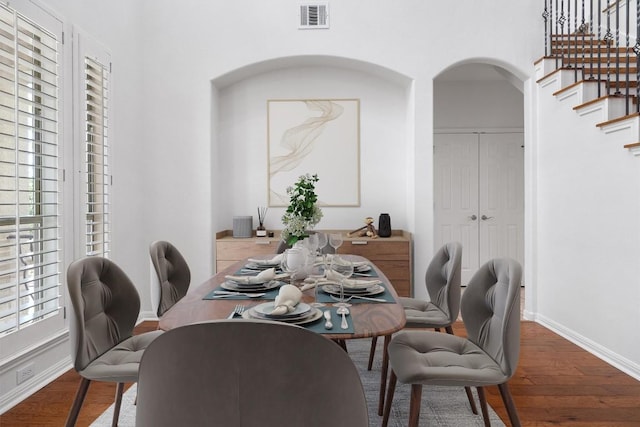 dining area featuring wood finished floors, visible vents, arched walkways, and stairway