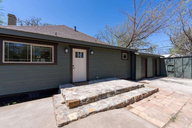 rear view of house with roof with shingles, a patio, and a chimney