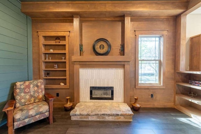 sitting room featuring dark wood-type flooring, a glass covered fireplace, and wood walls