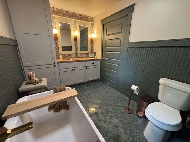 bathroom with a decorative wall, toilet, vanity, and a wainscoted wall