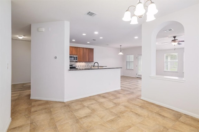 1317 Rimstone Dr, Cedar Park, TX 78613 - kitchen with stainless steel microwave, dark countertops, arched walkways, brown cabinetry, and decorative backsplash