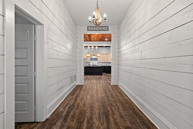 corridor featuring a chandelier, visible vents, wood walls, and dark wood-style floors