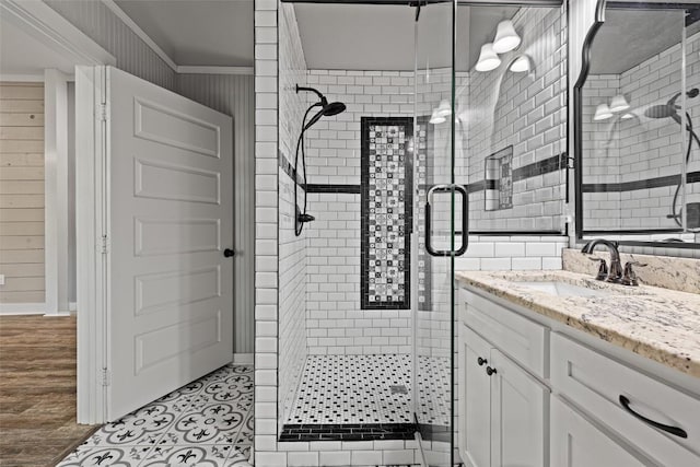 full bath with wooden walls, vanity, crown molding, baseboards, and a stall shower