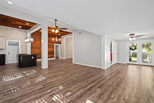 unfurnished living room with dark wood finished floors, wood walls, a ceiling fan, and decorative columns