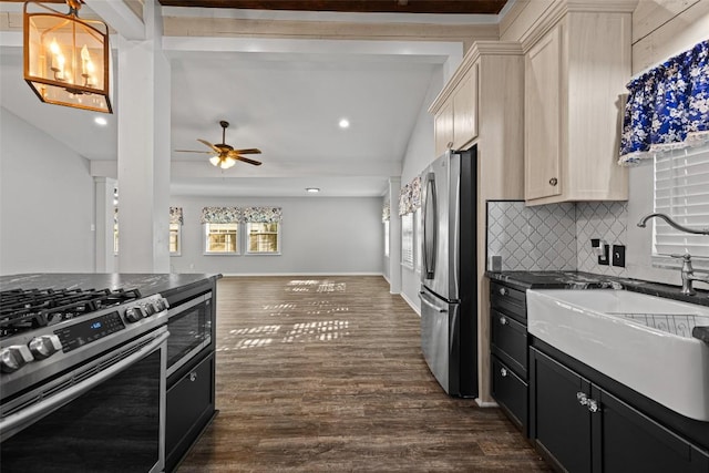 kitchen with stainless steel appliances, dark countertops, a sink, dark wood-type flooring, and tasteful backsplash