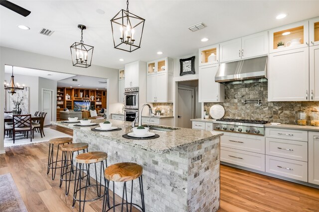 2305 Manana St, Austin, TX 78730 - kitchen with under cabinet range hood, a sink, appliances with stainless steel finishes, a chandelier, and white cabinetry