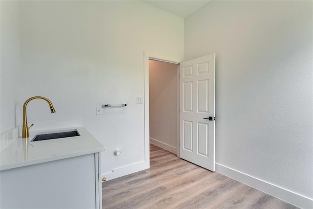 laundry area featuring baseboards, a sink, and light wood finished floors