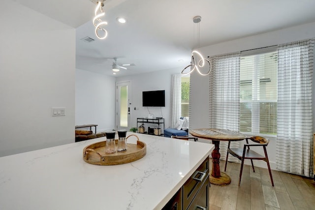 kitchen featuring light wood finished floors, visible vents, decorative light fixtures, light stone countertops, and open floor plan