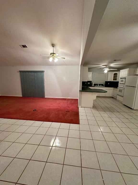 unfurnished living room with light carpet, a ceiling fan, visible vents, and light tile patterned floors