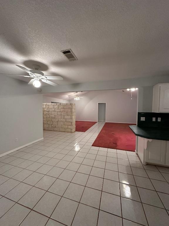 unfurnished living room featuring visible vents, light tile patterned floors, baseboards, a textured ceiling, and ceiling fan