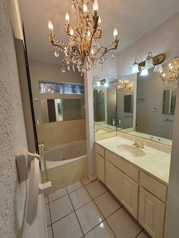 full bathroom featuring tile patterned flooring, an inviting chandelier, a textured wall, vanity, and a tub with jets